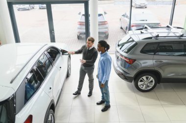 Erkek müşterinin portresi galeride profesyonel araba satıcısıyla konuşuyor. Yeni otomobil seçimi ve satın alma kavramı.