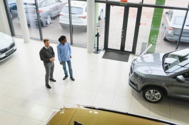 Erkek müşterinin portresi galeride profesyonel araba satıcısıyla konuşuyor. Yeni otomobil seçimi ve satın alma kavramı.