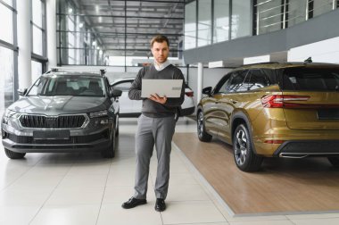 Araba satıcısı araba salonunda duruyor ve müşterilerin satışa çıkmasını bekliyor..