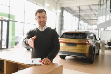 Araba satıcısı araba salonunda duruyor ve müşterilerin satışa çıkmasını bekliyor..