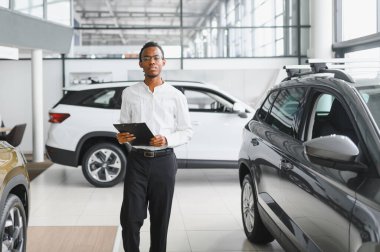 Afrikalı araba satıcısı araba galerisinde duruyor ve müşterilerin satışa çıkmasını bekliyor..