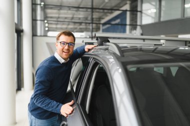 Bugün yeni bir araba aldım. Yerel bayilikte yeni arabasının yanında poz veren mutlu, olgun bir adamın portresi..