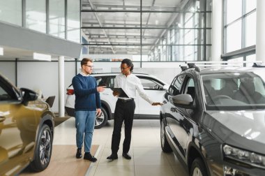 Erkek araba satıcısı, galeride dalgın genç bir müşteriyle sohbet ediyor. Satış merkezinden araba alırken adam dinliyor.