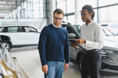 Erkek araba satıcısı araba galerisinde müşteriye araba seçmesinde yardımcı olur. Adam yeni araba alıyor..