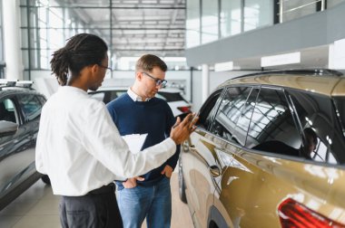 Erkek araba satıcısı araba galerisinde müşteriye araba seçmesinde yardımcı olur. Adam yeni araba alıyor..