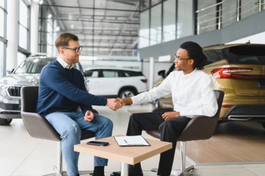 Otomobil salonunda erkek müşteriyle anlaşma yapan bir satıcı. Araba merkezinden yeni araç alan sakallı adam..