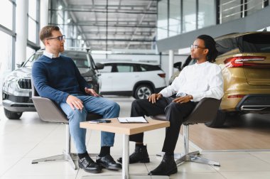 Otomobil salonunda erkek müşteriyle anlaşma yapan bir satıcı. Araba merkezinden yeni araç alan sakallı adam..