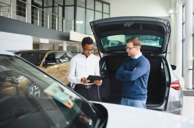 Erkek araba satıcısı araba galerisinde müşteriye araba seçmesinde yardımcı olur. Adam yeni araba alıyor..