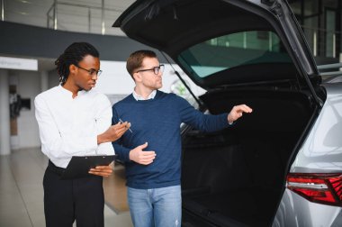 Erkek araba satıcısı, galeride dalgın genç bir müşteriyle sohbet ediyor. Satış merkezinden araba alırken adam dinliyor.