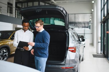 Erkek araba satıcısı, galeride dalgın genç bir müşteriyle sohbet ediyor. Satış merkezinden araba alırken adam dinliyor.