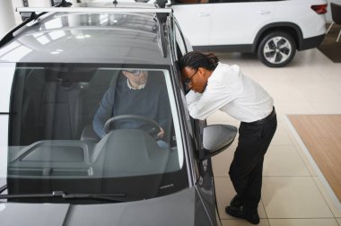 Erkek müşterinin portresi galeride profesyonel araba satıcısıyla konuşuyor. Yeni otomobil seçimi ve satın alma kavramı.