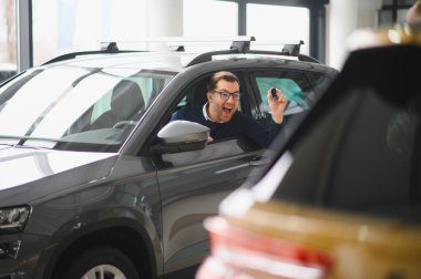 Genç adam yeni bir araç içinde araba Bayilik seçmektir.