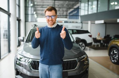 Genç adam yeni bir araç içinde araba Bayilik seçmektir.