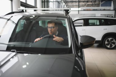 Genç adam yeni bir araç içinde araba Bayilik seçmektir.