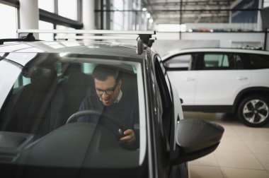 Genç adam yeni bir araç içinde araba Bayilik seçmektir.