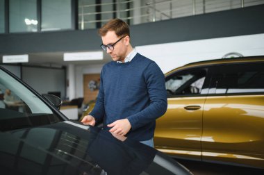 Genç adam yeni bir araç içinde araba Bayilik seçmektir.