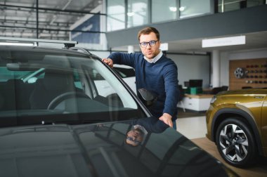 Genç adam yeni bir araç içinde araba Bayilik seçmektir.