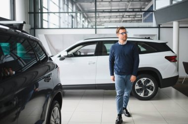 Genç adam yeni bir araç içinde araba Bayilik seçmektir.