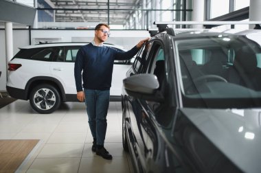 Genç adam yeni bir araç içinde araba Bayilik seçmektir.