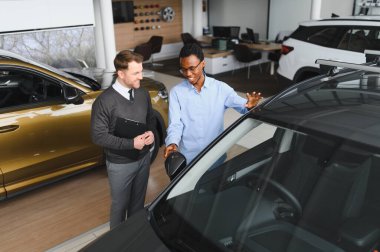 Erkek araba satıcısı araba galerisinde müşteriye araba seçmesinde yardımcı olur. Adam yeni araba alıyor..