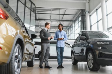 Erkek araba satıcısı, galeride dalgın genç bir müşteriyle sohbet ediyor. Satış merkezinden araba alırken adam dinliyor.