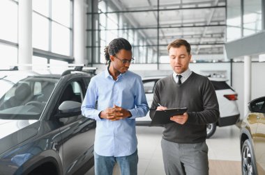 Erkek araba satıcısı araba galerisinde müşteriye araba seçmesinde yardımcı olur. Adam yeni araba alıyor..