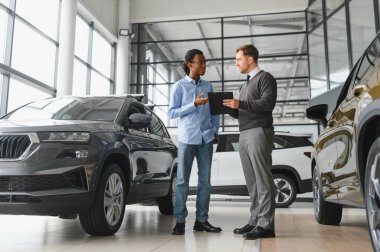 Erkek müşterinin portresi galeride profesyonel araba satıcısıyla konuşuyor. Yeni otomobil seçimi ve satın alma kavramı.