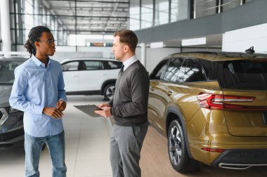 Erkek araba satıcısı araba galerisinde müşteriye araba seçmesinde yardımcı olur. Adam yeni araba alıyor..