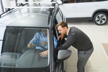 Erkek araba satıcısı araba galerisinde müşteriye araba seçmesinde yardımcı olur. Adam yeni araba alıyor..