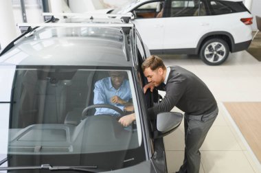 Erkek müşterinin portresi galeride profesyonel araba satıcısıyla konuşuyor. Yeni otomobil seçimi ve satın alma kavramı.