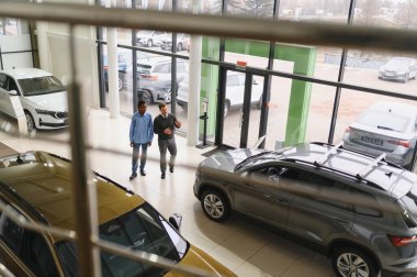 Erkek müşterinin portresi galeride profesyonel araba satıcısıyla konuşuyor. Yeni otomobil seçimi ve satın alma kavramı.