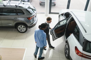 Erkek araba satıcısı, galeride dalgın genç bir müşteriyle sohbet ediyor. Satış merkezinden araba alırken adam dinliyor.