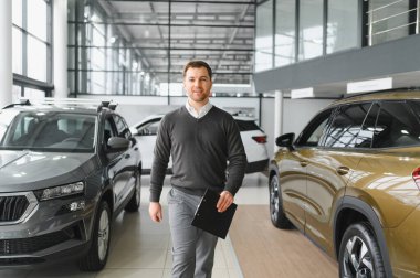 Araba satıcısı araba salonunda duruyor ve müşterilerin satışa çıkmasını bekliyor..