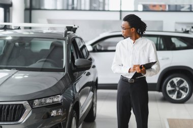 Afrikalı araba satıcısı araba galerisinde duruyor ve müşterilerin satışa çıkmasını bekliyor..