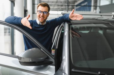 Genç adam yeni bir araç içinde araba Bayilik seçmektir.