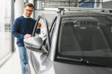 Genç adam yeni bir araç içinde araba Bayilik seçmektir.