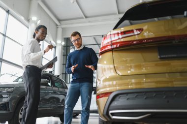 Erkek müşterinin portresi galeride profesyonel araba satıcısıyla konuşuyor. Yeni otomobil seçimi ve satın alma kavramı.