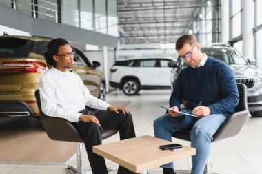 Otomobil salonunda erkek müşteriyle anlaşma yapan bir satıcı. Araba merkezinden yeni araç alan sakallı adam..