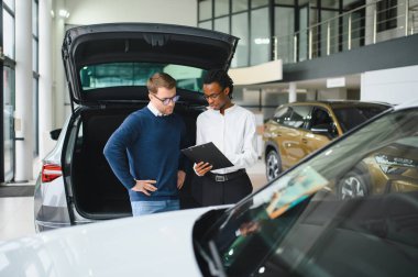 Erkek müşterinin portresi galeride profesyonel araba satıcısıyla konuşuyor. Yeni otomobil seçimi ve satın alma kavramı.