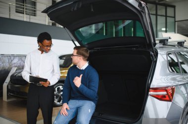 Erkek müşterinin portresi galeride profesyonel araba satıcısıyla konuşuyor. Yeni otomobil seçimi ve satın alma kavramı.