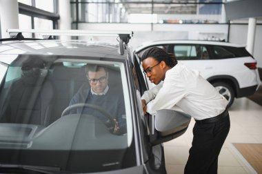 Erkek müşterinin portresi galeride profesyonel araba satıcısıyla konuşuyor. Yeni otomobil seçimi ve satın alma kavramı.