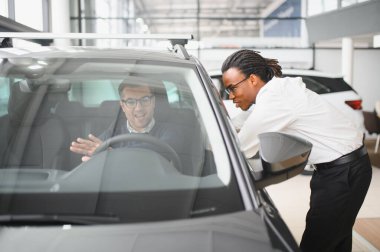 Erkek araba satıcısı araba galerisinde müşteriye araba seçmesinde yardımcı olur. Adam yeni araba alıyor..