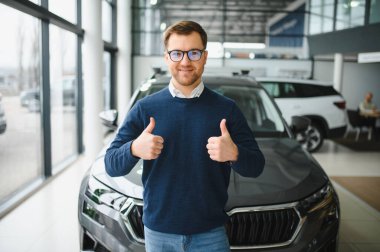 Bugün yeni bir araba aldım. Yerel bayilikte yeni arabasının yanında poz veren mutlu, olgun bir adamın portresi..