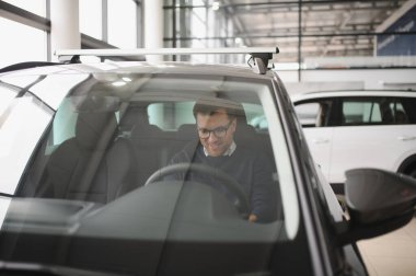 Genç adam yeni bir araç içinde araba Bayilik seçmektir.