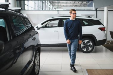 Genç adam yeni bir araç içinde araba Bayilik seçmektir.