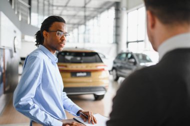 Otomobil salonunda erkek müşteriyle anlaşma yapan bir satıcı. Araba merkezinden yeni araç alan sakallı adam..