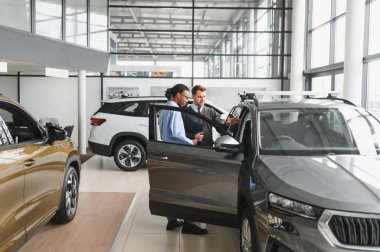 Erkek müşterinin portresi galeride profesyonel araba satıcısıyla konuşuyor. Yeni otomobil seçimi ve satın alma kavramı.