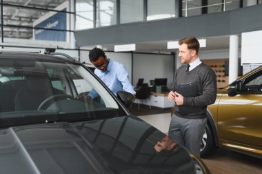 Erkek müşterinin portresi galeride profesyonel araba satıcısıyla konuşuyor. Yeni otomobil seçimi ve satın alma kavramı.