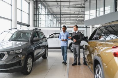 Erkek araba satıcısı, galeride dalgın genç bir müşteriyle sohbet ediyor. Satış merkezinden araba alırken adam dinliyor.