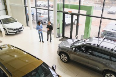 Erkek araba satıcısı araba galerisinde müşteriye araba seçmesinde yardımcı olur. Adam yeni araba alıyor..